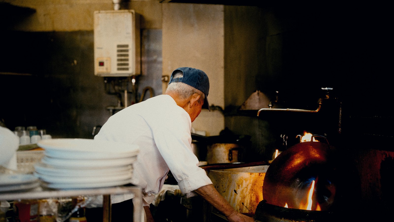 Een kok aan het werk in een open keuken, tussen pannen en stapels borden