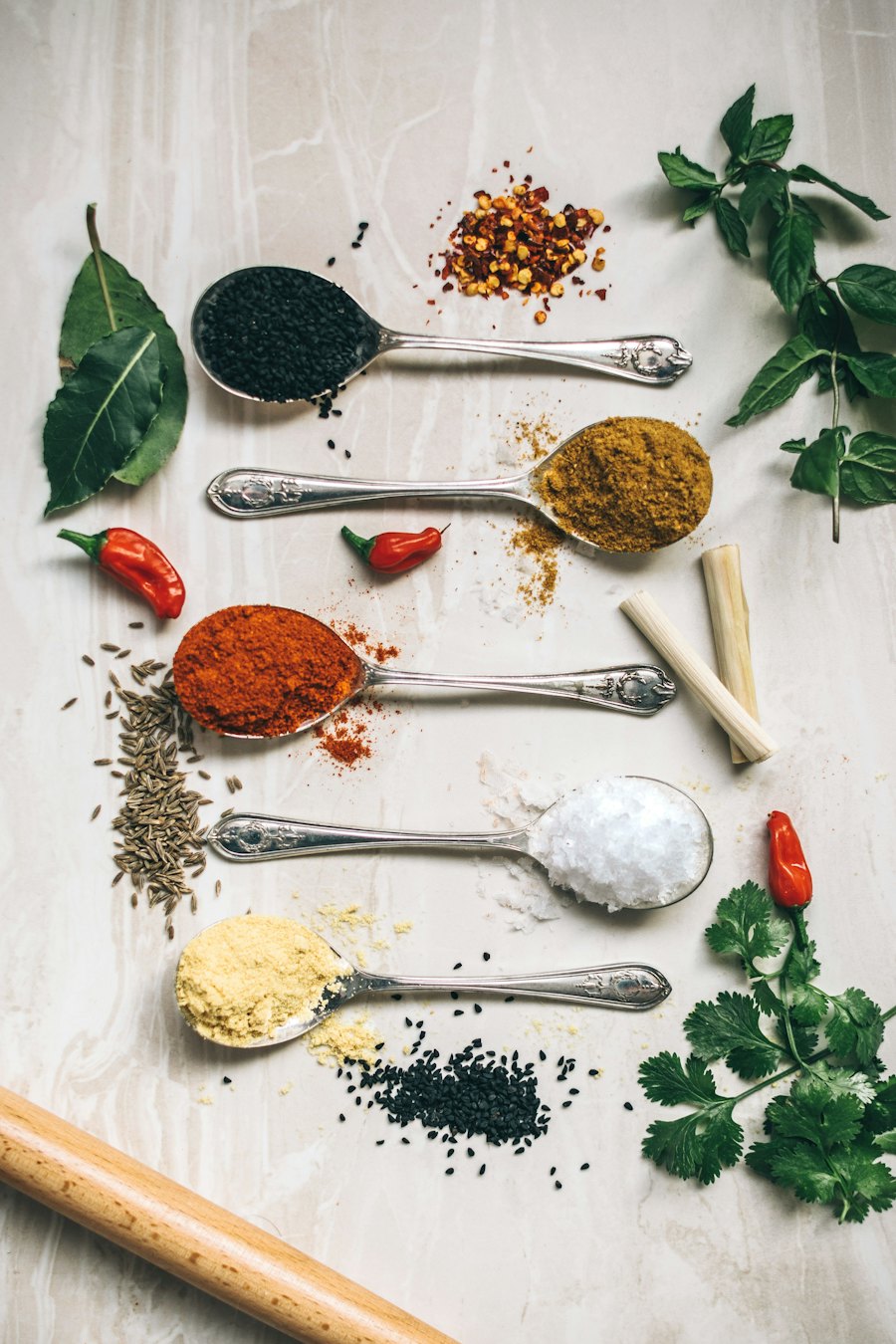 Vijf lepels met specerijen op een marmeren blad, met chili en verse kruiden